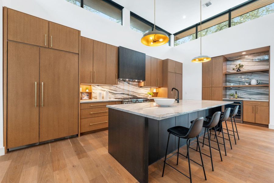 Two tone kitchen with light stone counters, decorative light fixtures, a kitchen breakfast bar, light wood-style floors, and a high ceiling