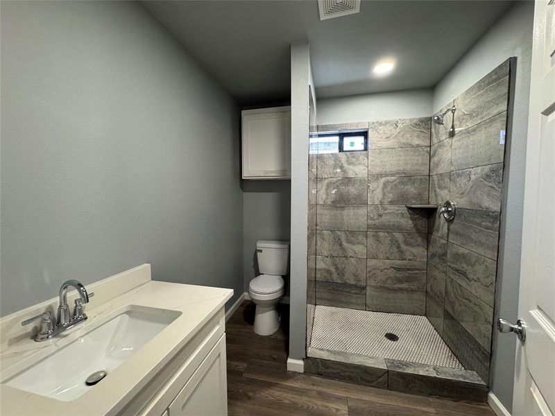 Bathroom with hardwood / wood-style flooring, vanity, toilet, and a tile shower