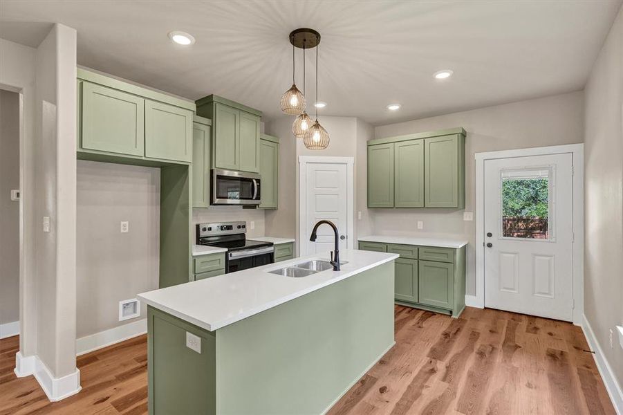 Kitchen with green cabinets, appliances with stainless steel finishes, pendant lighting, recessed lighting, and light wood finished floors Kitchen with green cabinets, appliances with stainless steel finishes, pendant lighting, recessed lighting, and light wood finished floors