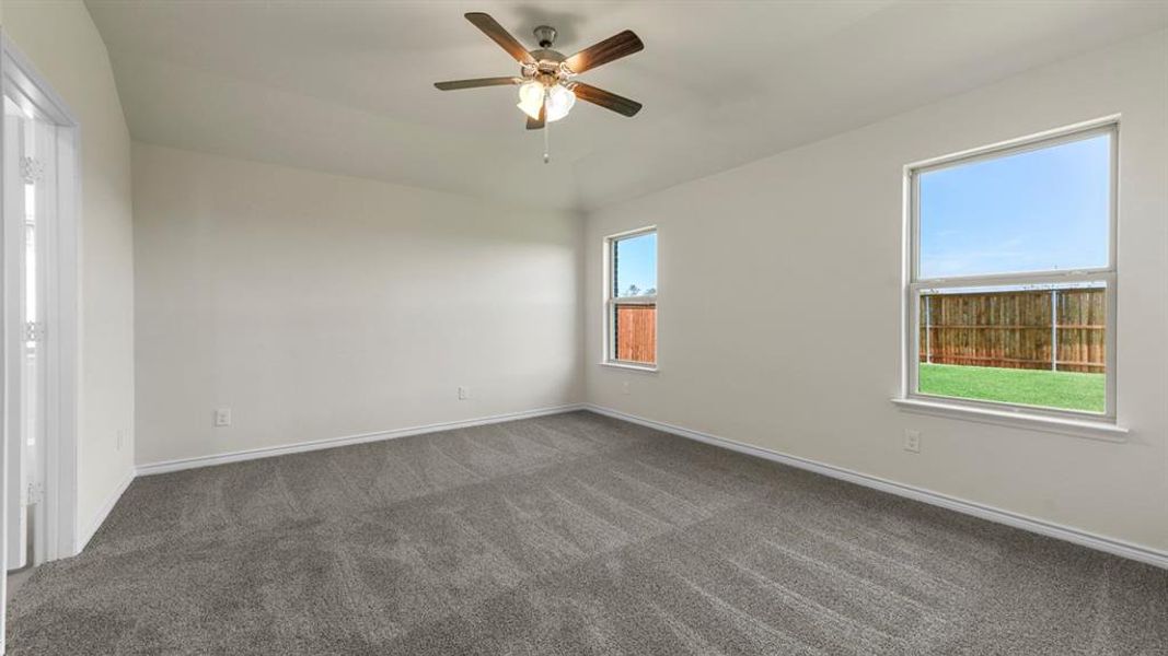 This room features neutral-toned walls, a textured carpet, and windows providing views of a fenced yard