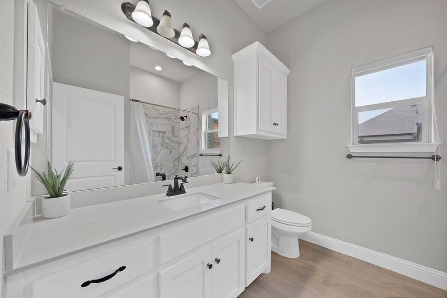 Full bath with toilet, vanity, curtained shower, wood finished floors, and baseboards Full bath with toilet, vanity, curtained shower, wood finished floors, and baseboards