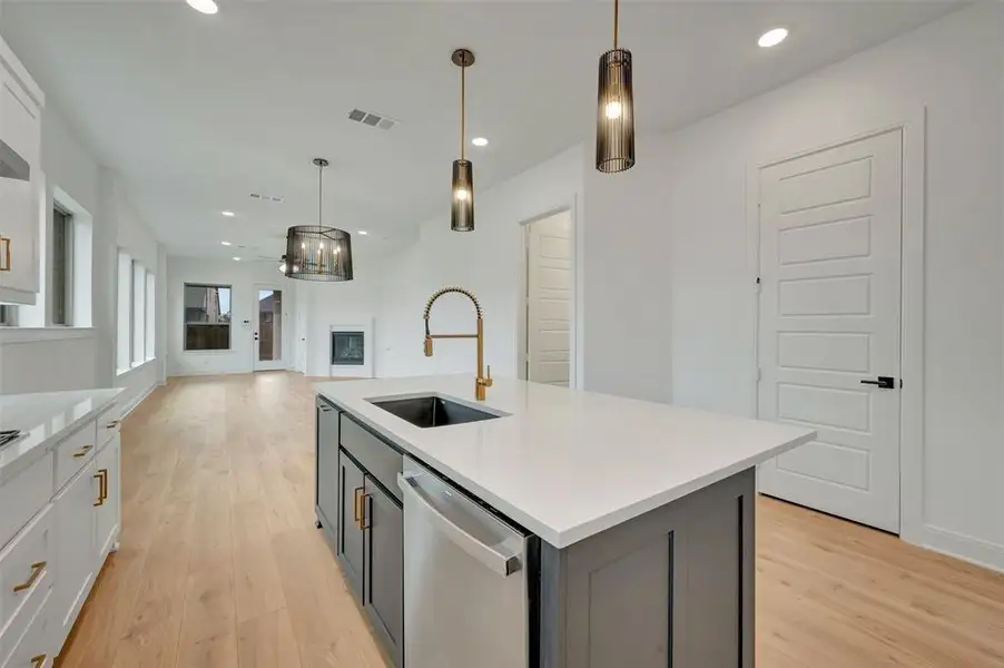 Kitchen island featuring a white countertop, undermount sink with a gold-tone faucet, and dark cabinetry