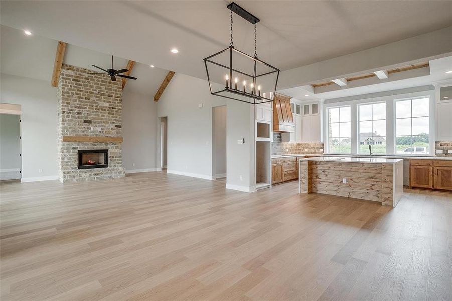 Kitchen with a center island, a fireplace, light wood-type flooring, ceiling fan with notable chandelier, and tasteful backsplash