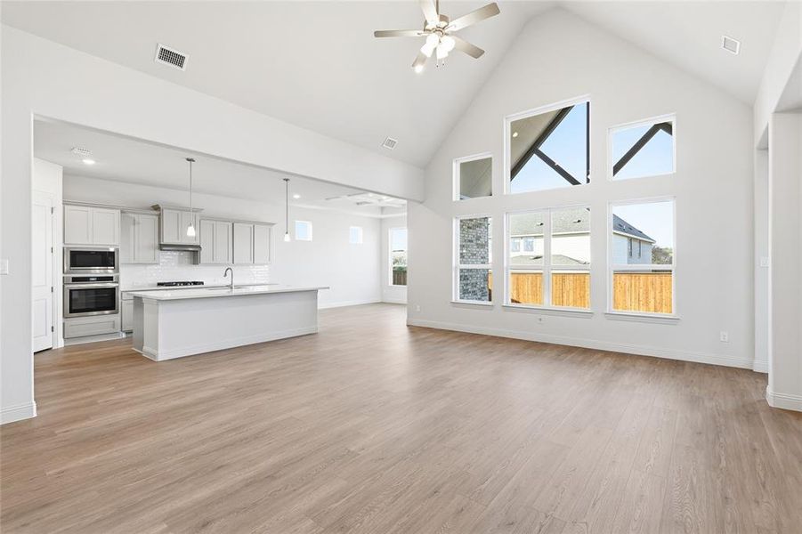 Unfurnished living room featuring ceiling fan, high vaulted ceiling, and light wood-type flooring Unfurnished living room featuring ceiling fan, high vaulted ceiling, and light wood-type flooring