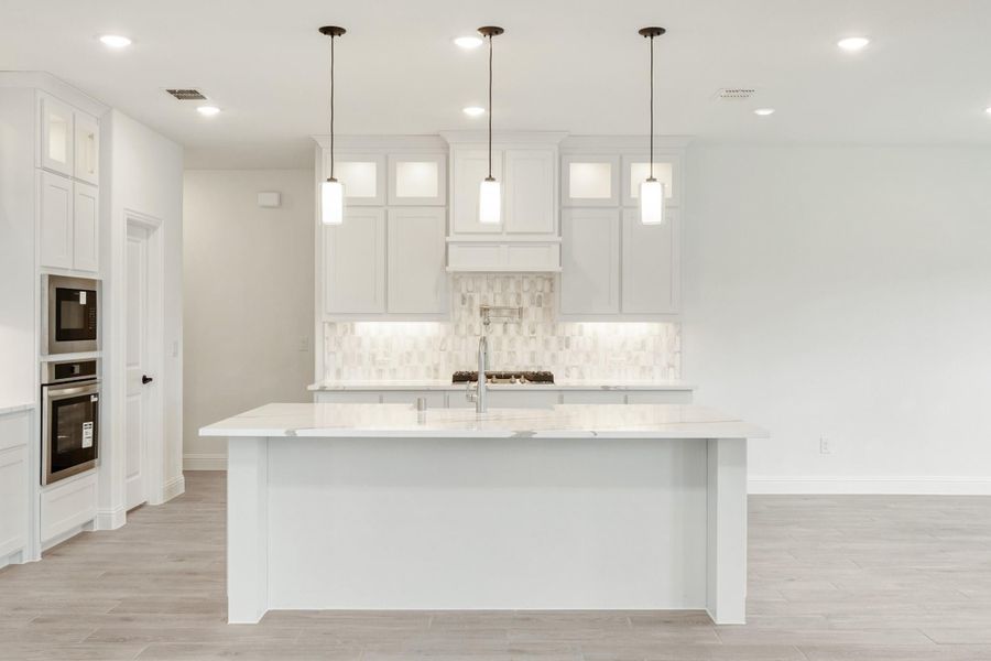 White kitchen with large island, pendant lights, tile backsplash, and built-in double ovens