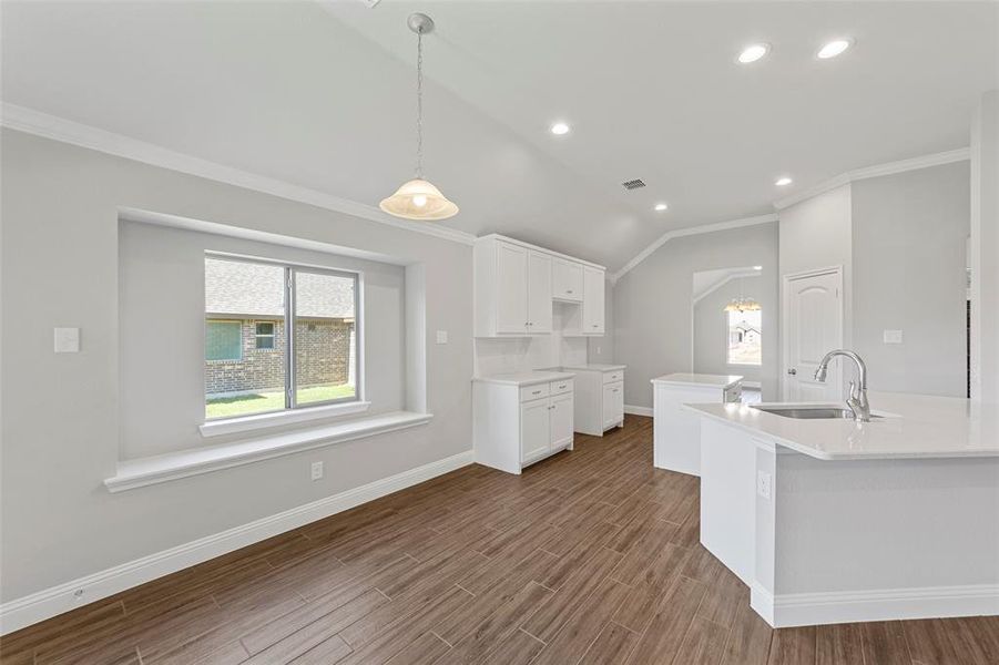 Kitchen featuring sink, hardwood / wood-style floors, an island with sink, vaulted ceiling, and white cabinets