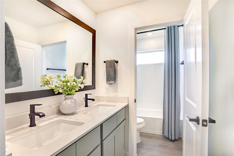 This bathroom features a modern double vanity with sleek black faucets, a large framed mirror, and elegant grey cabinetry. This bathroom features a modern double vanity with sleek black faucets, a large framed mirror, and elegant grey cabinetry.