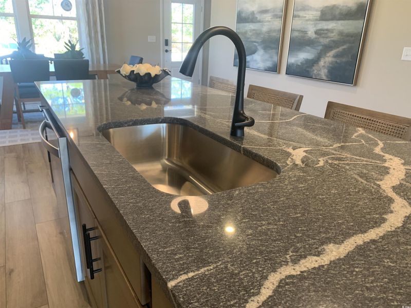 Kitchen view of a kitchen bar, dark stone counters, wood finished floors, and stainless steel dishwasher