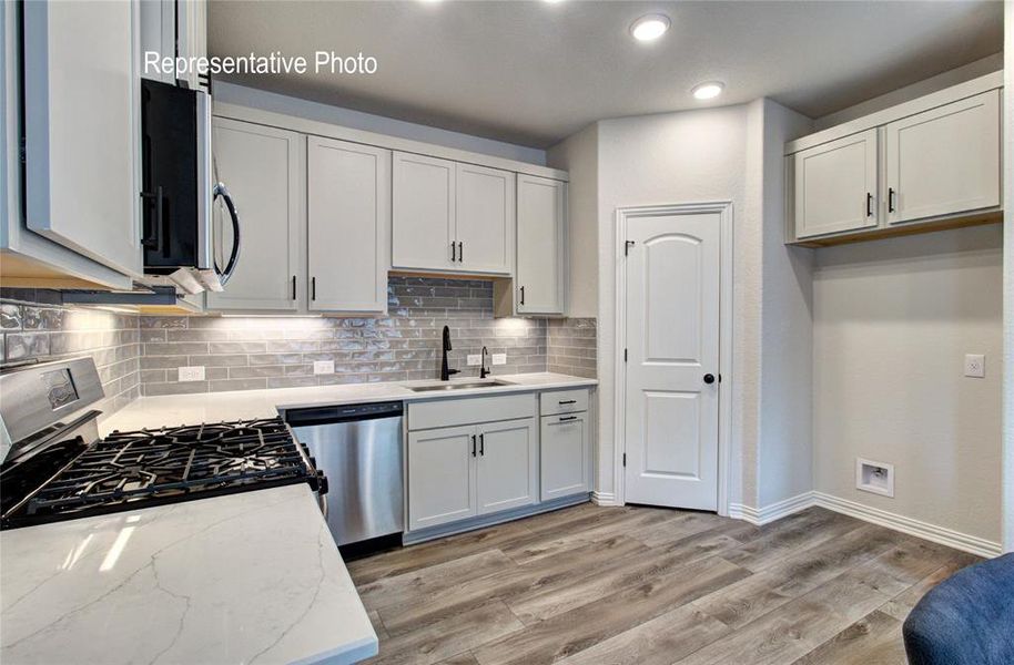 Kitchen featuring white cabinetry, stainless steel appliances, quartz countertops, a subway tile backsplash, and wood-finish flooring