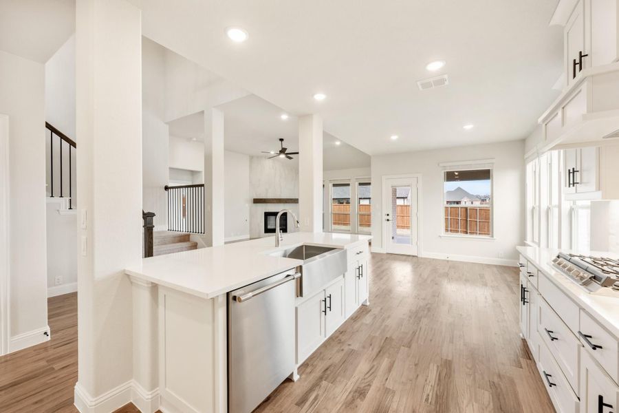 Open kitchen with white cabinets, large island, farmhouse sink, and light wood floors open to living area