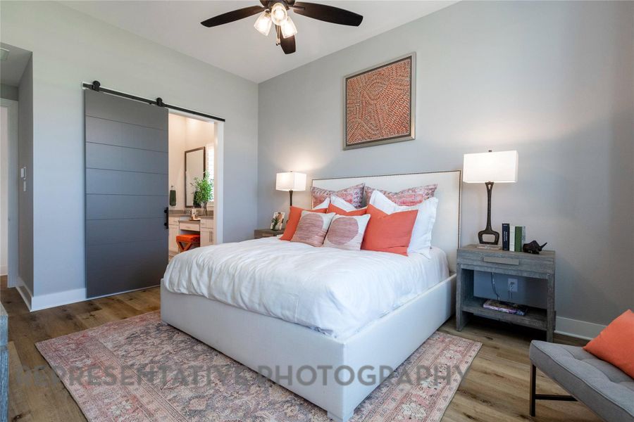 Bedroom with a barn door, connected bathroom, wood finished floors, and ceiling fan Bedroom with a barn door, connected bathroom, wood finished floors, and ceiling fan