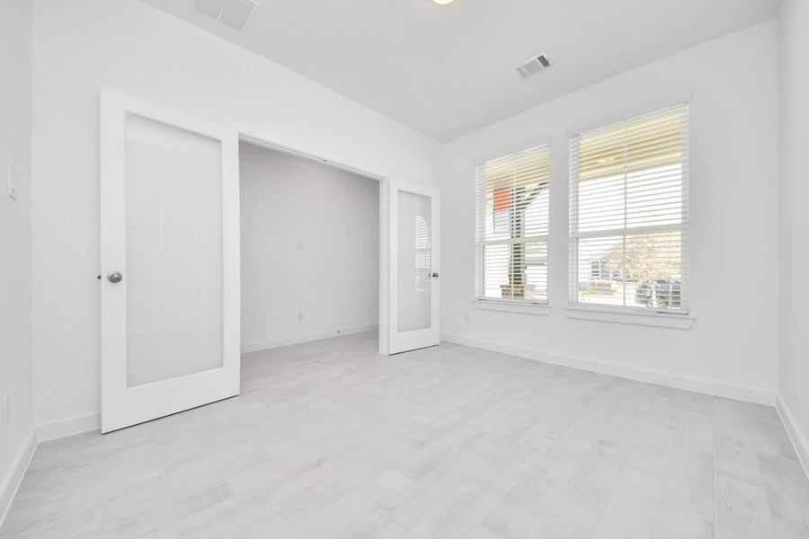 Experience the perfect blend of sophistication and warmth in this home office, boasting elegant wood-look tile flooring and flooded with natural light from expansive windows and French doors.