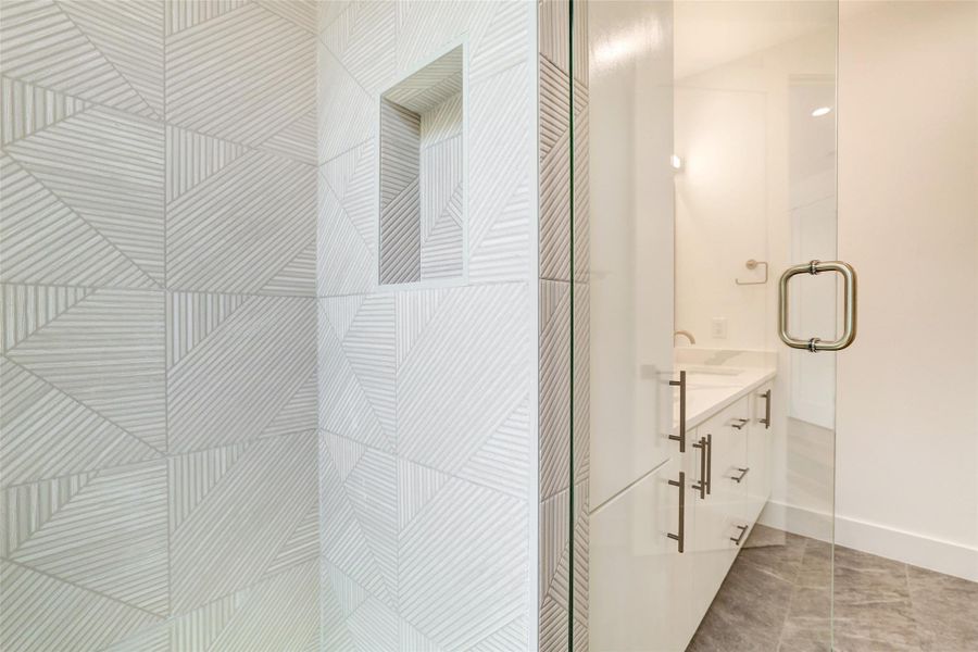 Full bathroom with tiled shower, vanity, baseboards, and tile patterned floors