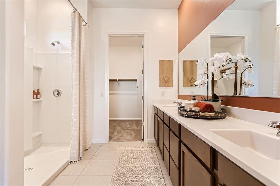 Full bath with light tile patterned floors, double vanity, a stall shower, and a walk in closet