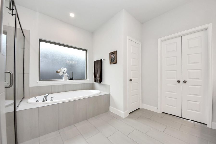 This bathroom combines modern design with functionality, offering a built-in bathtub, frosted window for natural light and privacy, sleek tile flooring, and ample double-door storage. Neutral tones and clean lines enhance the tranquil ambiance.