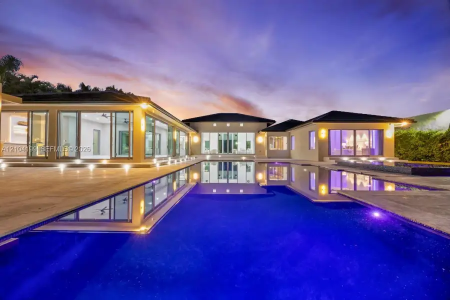 Contemporary residence featuring an infinity-edge pool, stone-paved patio, recessed exterior lighting, and floor-to-ceiling glass sliding doors