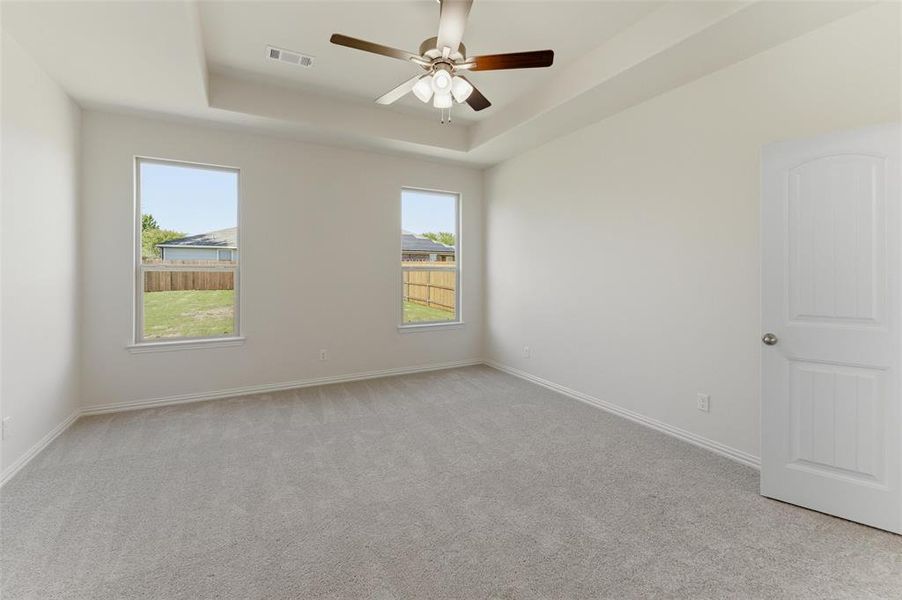 Empty room featuring light carpet, a tray ceiling, and a ceiling fan
