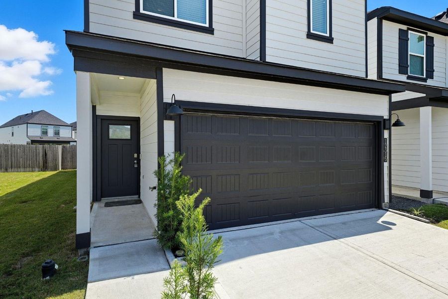 The two-car garage and covered entryway, highlight the modern black door, exterior lighting, and low-maintenance landscaping.
