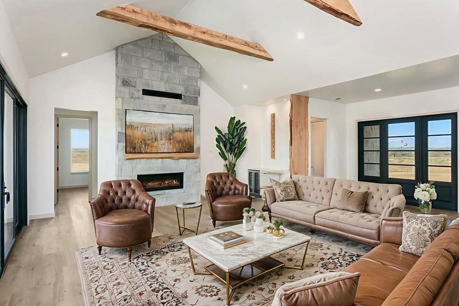 Living room featuring healthy amount of natural light, wood finished floors, a fireplace, beamed ceiling, and high vaulted ceiling Living room featuring healthy amount of natural light, wood finished floors, a fireplace, beamed ceiling, and high vaulted ceiling