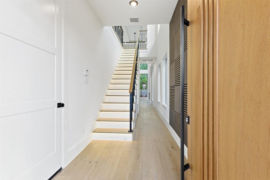 The entryway showcases wide-plank wood flooring, a textured wood accent wall, and a staircase with integrated tread lighting.