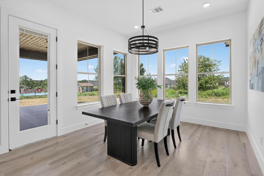 Bright dining space featuring a modern chandelier, light wood-finish flooring, and multiple windows