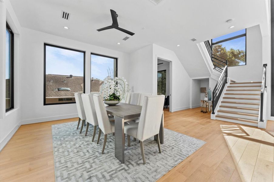 Bright dining area with modern design, featuring large windows, a sleek dining table, and an elegant staircase. The natural light and open layout create an inviting atmosphere.