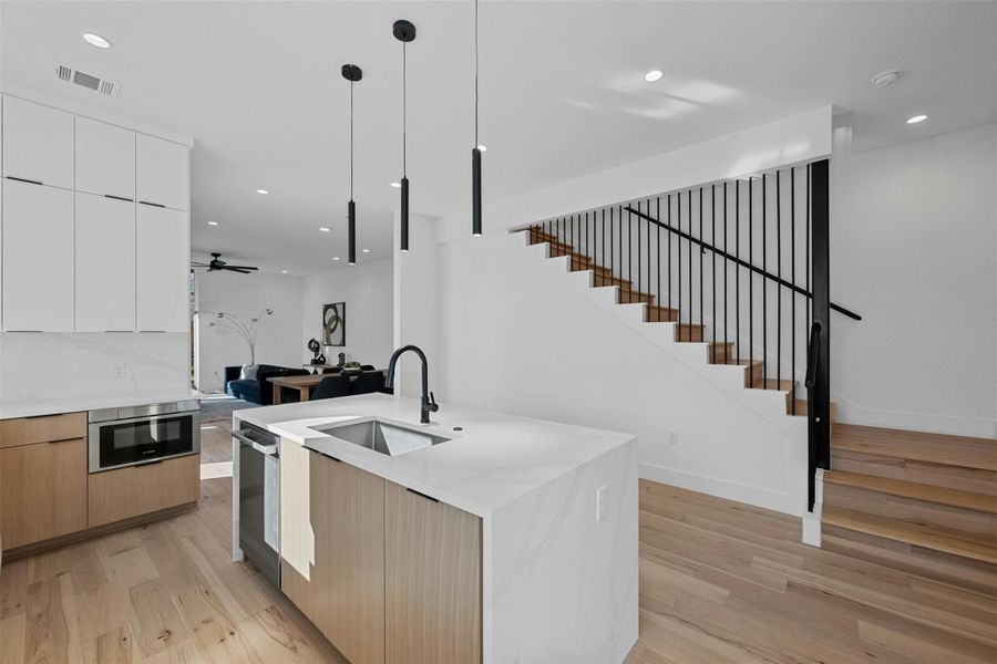 Kitchen with modern cabinets, an island with sink, light wood-type flooring, open floor plan, and ceiling fan Kitchen with modern cabinets, an island with sink, light wood-type flooring, open floor plan, and ceiling fan