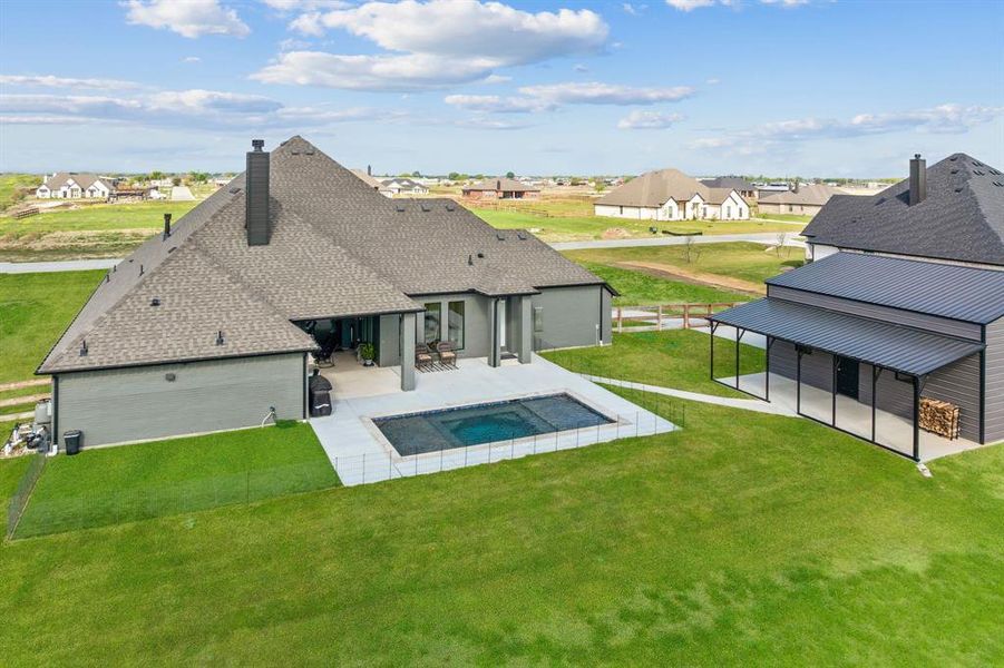 Back of property featuring a patio, a lawn, a shingled roof, and a residential view
