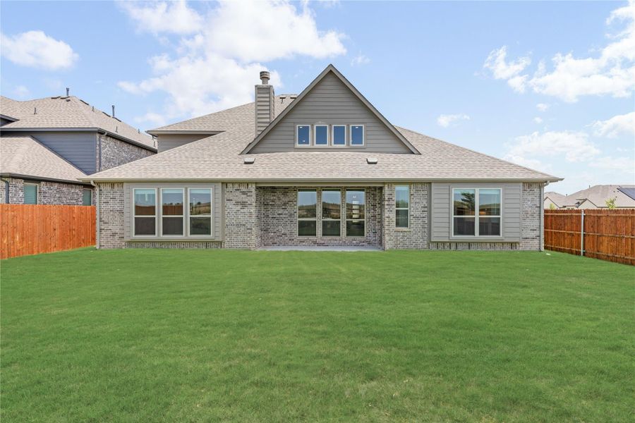 Rear view of brick home with large windows, wood privacy fence, and spacious green backyard lawn