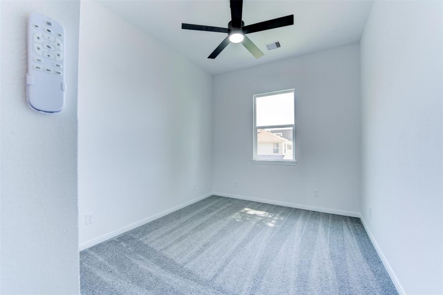 Additional secondary bedroom with plush carpet, a ceiling fan with integrated light kit, and a large window bringing in natural light. Clean, neutral finishes create a bright and comfortable space.