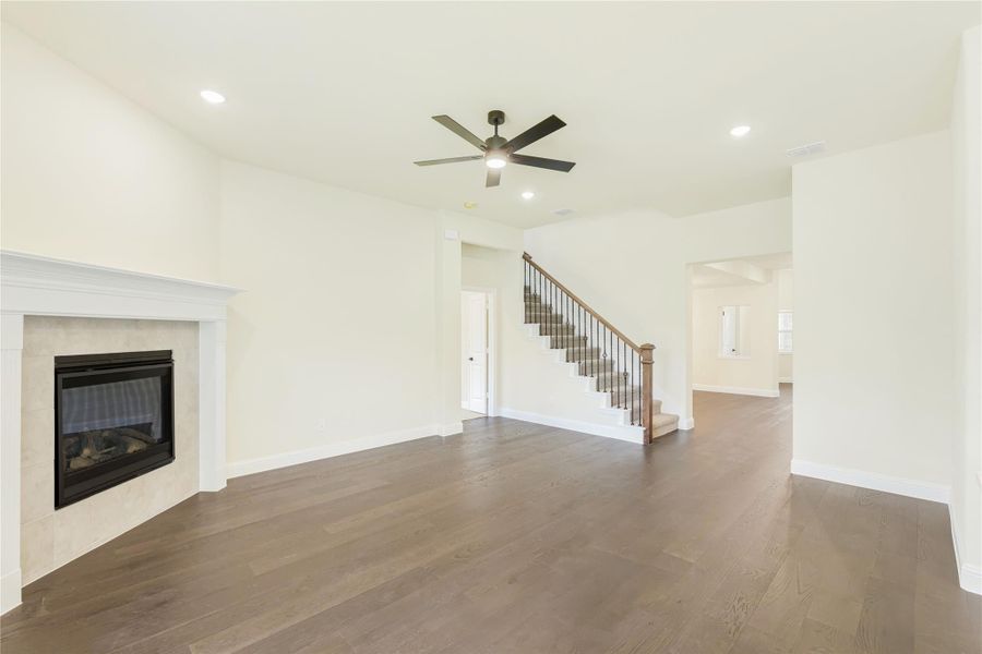 Open living room with hardwood floors, tile fireplace, ceiling fan, and staircase with wood railing Open living room with hardwood floors, tile fireplace, ceiling fan, and staircase with wood railing