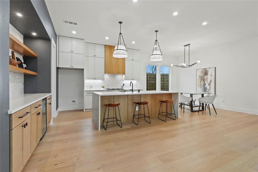 Dual tone kitchen featuring a kitchen bar, two tone cabinets, backsplash, light wood-type flooring, and a large island with sink