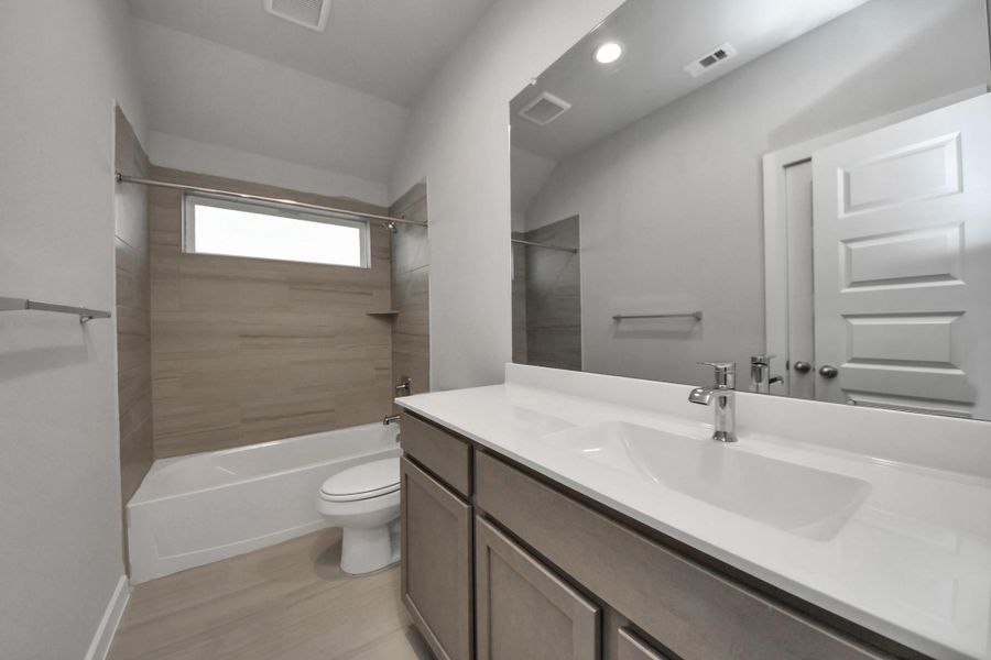 Secondary bath features tile flooring, bath/shower combo with tile surround, light stainedwood cabinets, beautiful light countertop. Sample photo of completed home with similar floor plan. Actual colors and selections may vary.