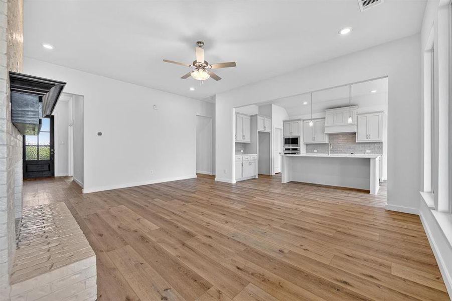 Spacious open-concept living area featuring wood-finish flooring, a white brick fireplace with a dark mantel, and recessed lighting