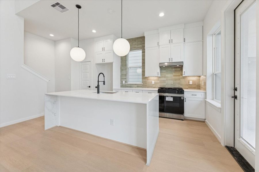 Large waterfall-edge island anchors the kitchen, offering generous workspace and seating. Matte black fixtures, quartz surfaces, and subtle tile accents lend a polished, modern aesthetic while maintaining a comfortable, inviting feel that connects seamlessly to the living area.