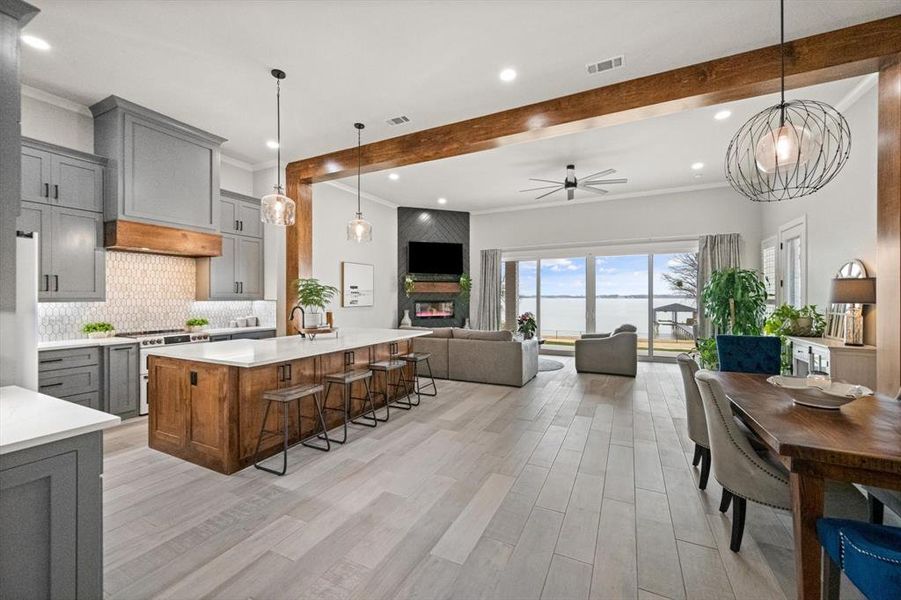 Open area of kitchen, dining and living areas featuring painted & stained cabinets, ornamental molding, recessed and pendant lighting