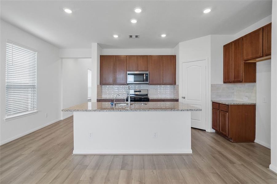 This spacious kitchen features high ceilings, recessed lighting, stained wood cabinets, granite countertops, SS appliances, modern tile backsplash, huge granite kitchen island with large sink and space for breakfast bar, and a pantry all overlooking your huge family room.