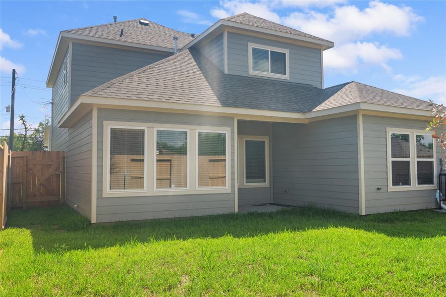 This photo showcases the back exterior of a two-story home with gray siding and a fenced backyard. The house features large windows and a small covered patio, perfect for outdoor relaxation.