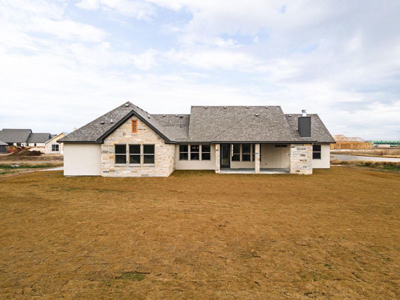Back of property featuring stone siding, a patio area, a chimney, a yard, and a shingled roof