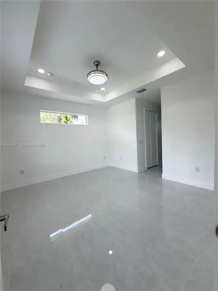 Tray ceiling with recessed lighting, large-format tile flooring, central ceiling fan, and horizontal clerestory window
