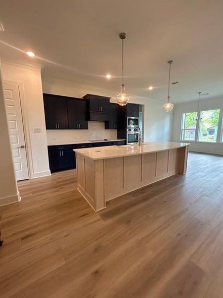 Kitchen featuring pendant lighting, a large island with sink, light wood-type flooring, backsplash, and light stone counters