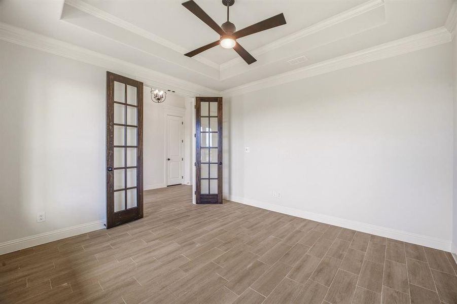Empty room featuring french doors, a ceiling fan, wood finish floors, a raised ceiling, and ornamental molding