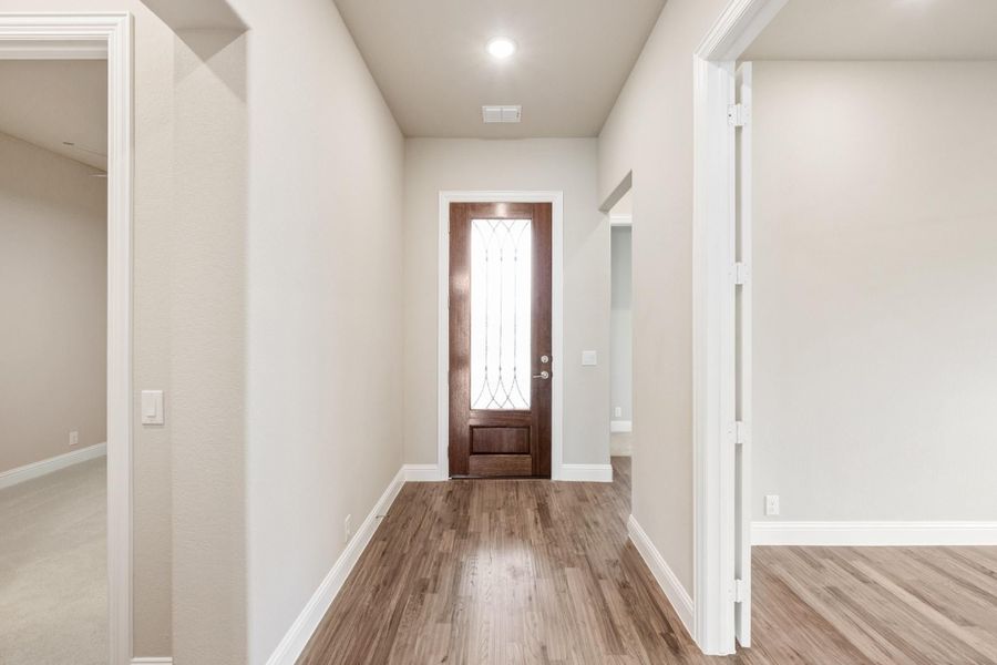 Entryway hallway with wood floors, white walls, and dark wood front door with glass panel