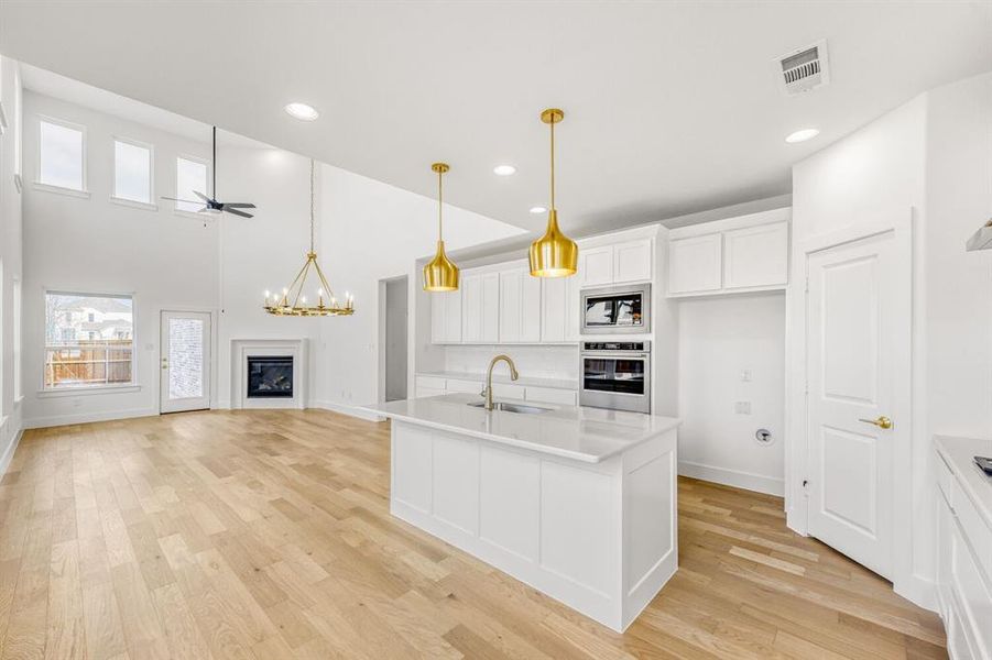 Kitchen with white cabinetry, a high ceiling, a kitchen island with sink, suspended lighting, and light wood finished floors