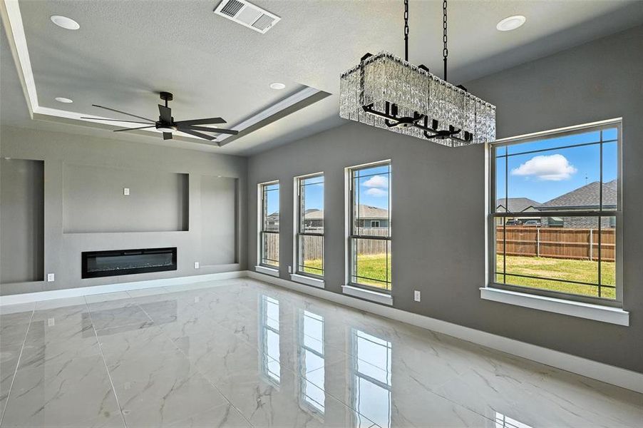 Unfurnished living room featuring marble finish floors, a glass covered fireplace, ceiling fan, a raised ceiling, and recessed lighting Unfurnished living room featuring marble finish floors, a glass covered fireplace, ceiling fan, a raised ceiling, and recessed lighting