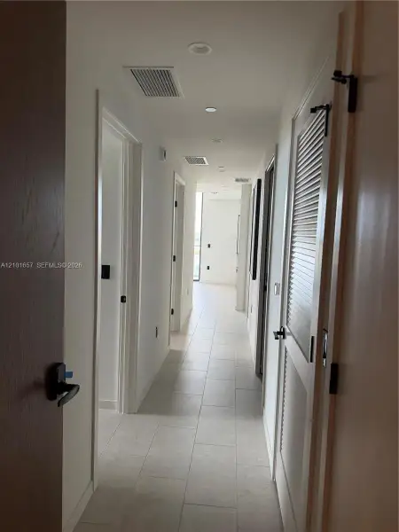 Hallway featuring large-format ceramic tile flooring, recessed ceiling lighting, and matte black hardware on solid-core wood doors, including a louvered closet door
