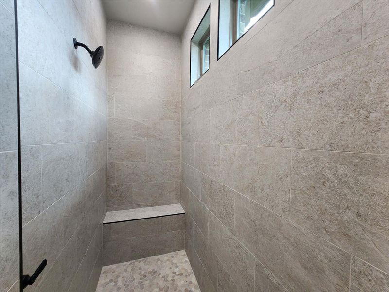 Tiled shower enclosure featuring a built-in bench, matte black fixtures, and high transom windows