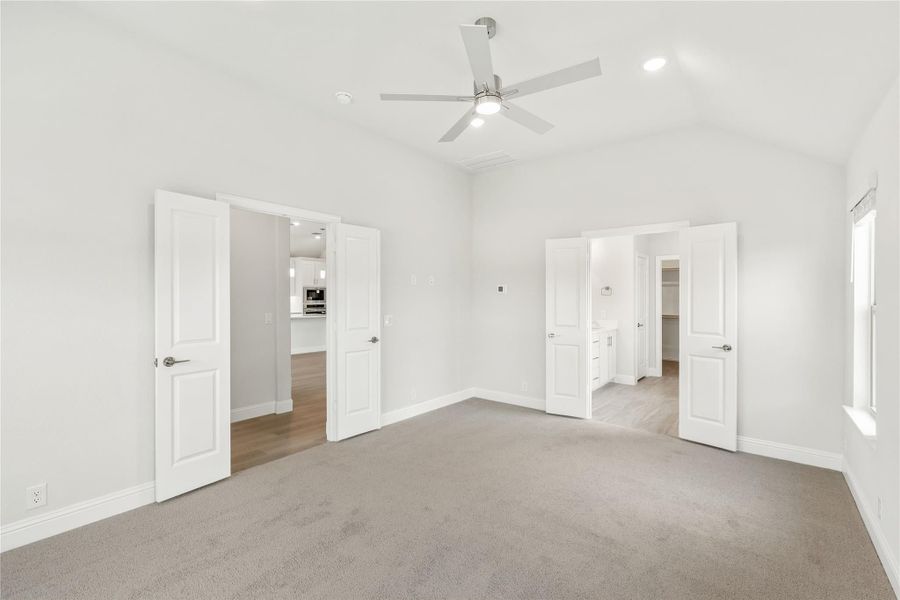 Empty bedroom with vaulted ceiling, ceiling fan, carpet floors, and doors leading to bathroom and closet Empty bedroom with vaulted ceiling, ceiling fan, carpet floors, and doors leading to bathroom and closet