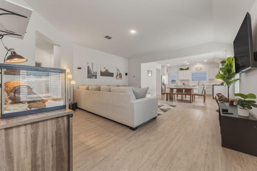 This expansive open-concept living area features light-toned flooring, a light-colored couch, and white walls, with recessed lighting providing illumination