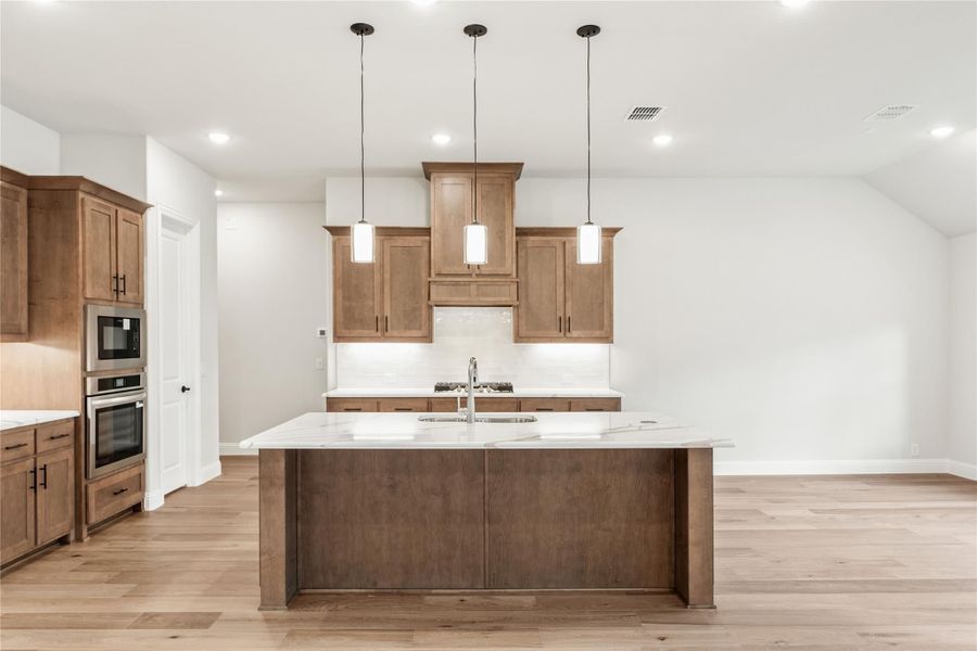 Kitchen with large center island, white quartz countertops, brown wood cabinets, pendant lights, and stainless steel appliances